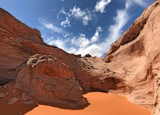 Orange sand below swirling cliffs